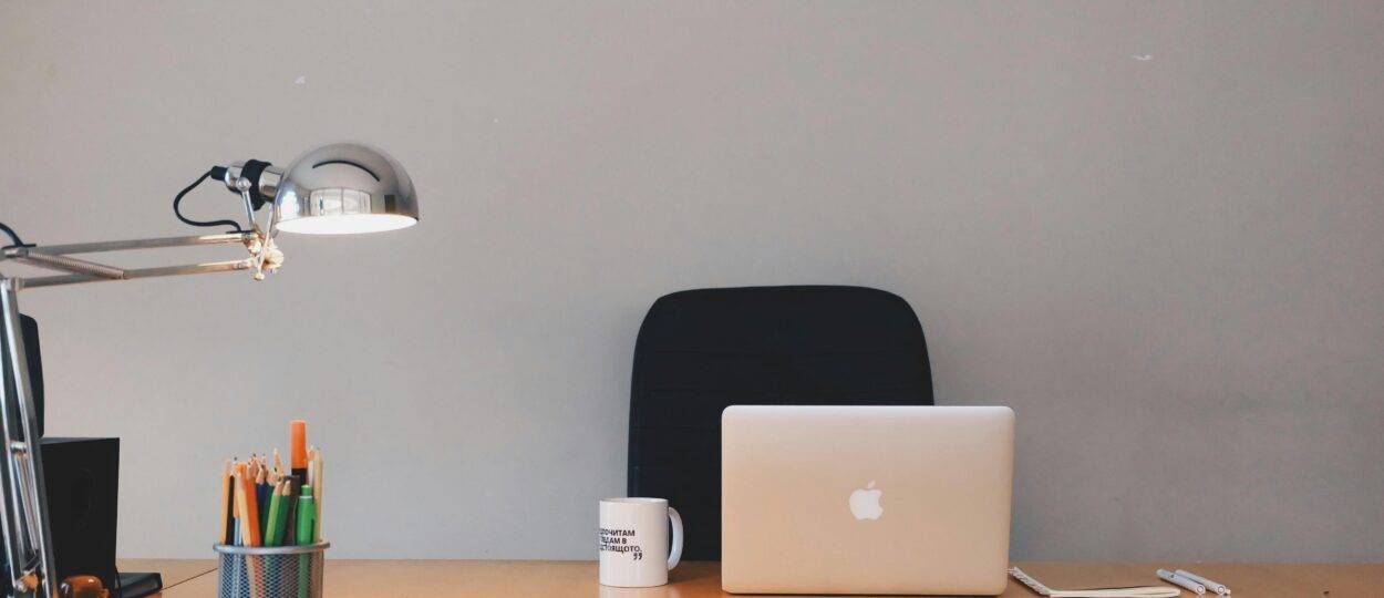 A tidy minimalist office setup featuring a laptop, desk lamp, and stationery.
