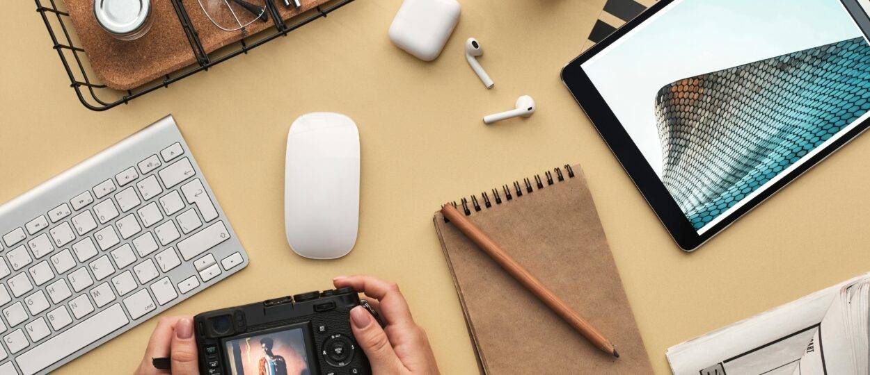 Overhead view of a modern workspace featuring tech gadgets, a camera, and a notepad.