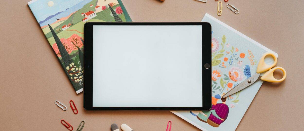 Flat lay of colorful stationery with tablet, notebooks, and scissors, ideal for education themes.