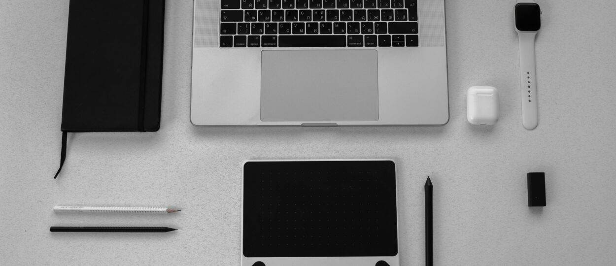 Black and white flatlay of stylish tech gadgets including laptop and smartwatch on a desk.