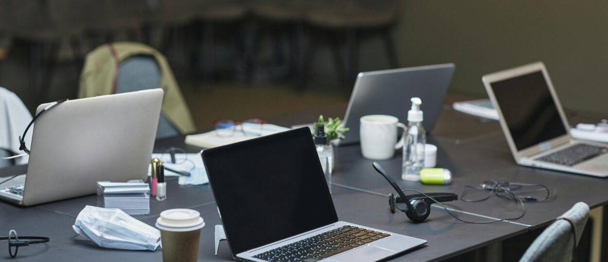 A cluttered office desk setup featuring multiple laptops, coffee cup, and office supplies for a busy workday.